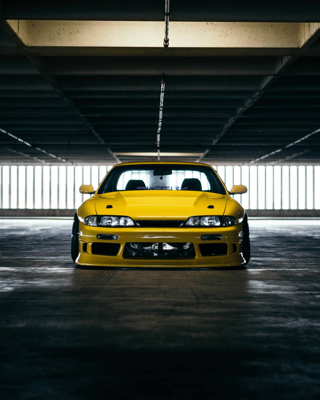 Yellow Nissan Silvia S14 sitting low in a parking garage