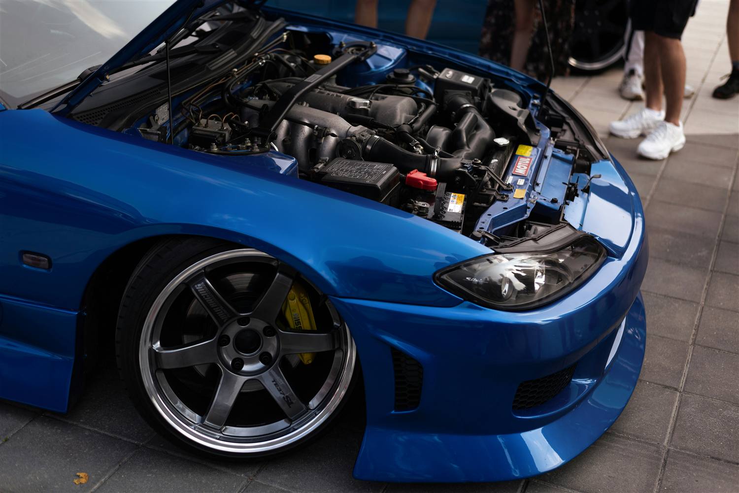 Engine bay of a blue Nissan Silvia S15 beside a bronze TE37 wheel
